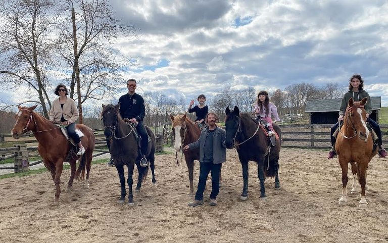 Our whole family sitting on horses and posing for a photo. There is a man standing in front of Zuzu and Lamp's horses and holding the reigns. 