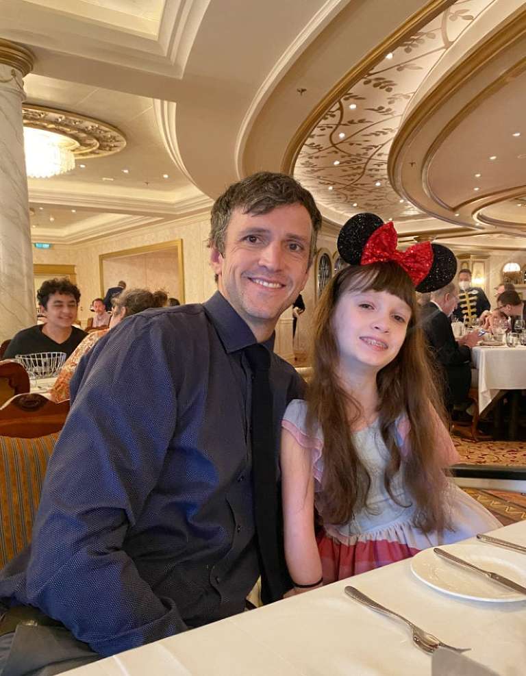 My husband, a white man with dark hair, and my middle daughter, a white girl with long brown hair, sitting next to each other at dinner posing for a picture.